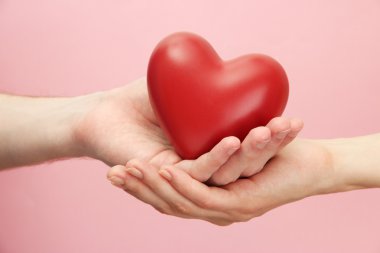 kadın ve adam ellerini, pembe bir arka plan üzerinde kırmızı kalp