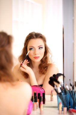 Genç ve güzel bir kadın aynanın yanında makyaj yapıyor.