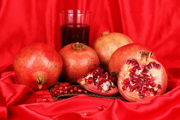 Granadas maduras con vaso de jugo de granada sobre fondo de tela roja — Foto de Stock