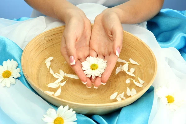 Manos de mujer con cuenco de madera de agua con flores, sobre fondo azul —  Fotos de Stock