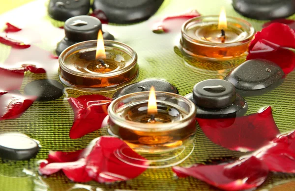 Piedras de spa con pétalos de rosa y velas en agua en placa —  Fotos de Stock