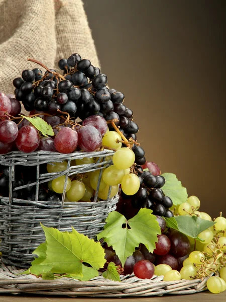 Assortment of ripe sweet grapes in basket, on brown background — Stock Photo, Image