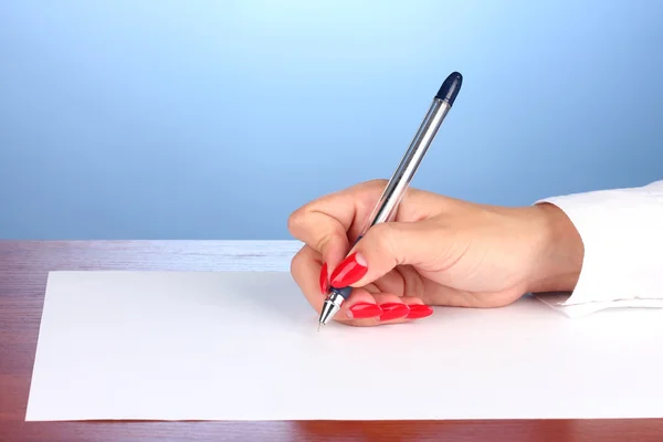 Manos escribiendo sobre papel sobre fondo azul — Foto de Stock