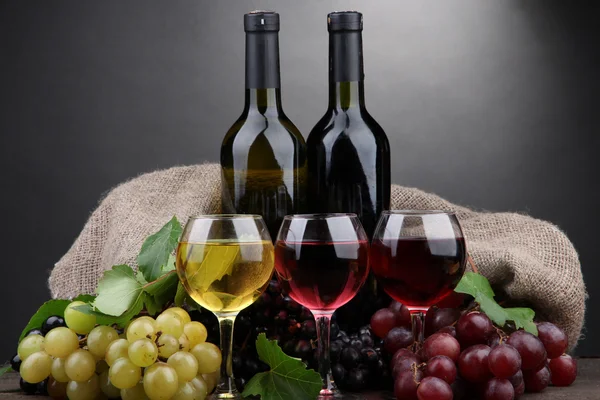 Bottiglie e calici di vino e uva su fondo grigio — Foto Stock