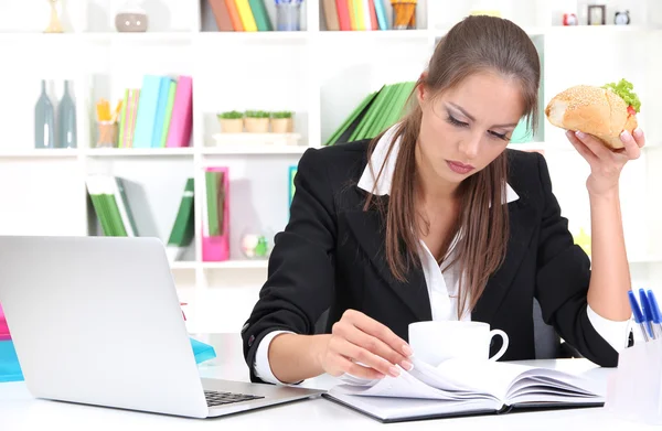 Donna d'affari mangiare hamburger sul posto di lavoro — Foto Stock