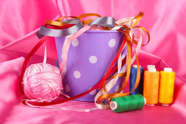Color bucket with multicolor ribbons and thread on color fabric background — Stock Photo, Image