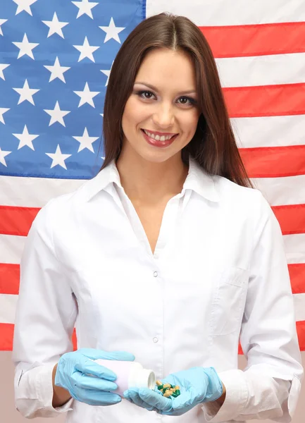 Portrait d'une femme médecin ou scientifique montrant et analysant des pilules sur fond de drapeau américain — Photo