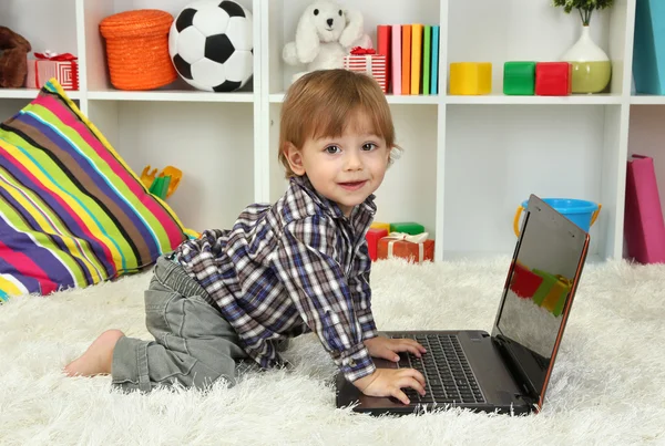 Roztomilý malý chlapec a notebook v místnosti — Stock fotografie