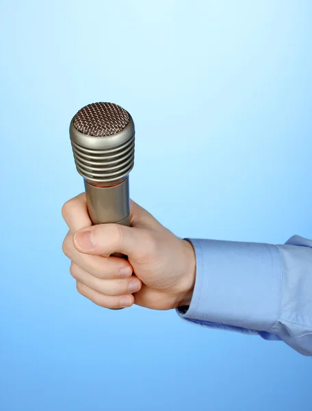 Male hand with microphone on blue background — Stock Photo, Image