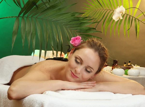 Hermosa joven en el salón de spa con piedras de spa, sobre fondo verde — Foto de Stock