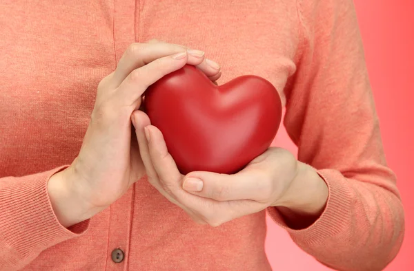 Red heart in woman hands, on red background — Stock Photo, Image