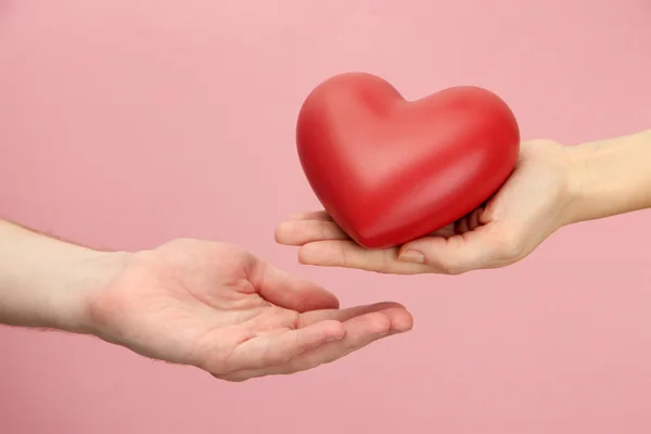 Corazón rojo en manos de hombre y mujer, sobre fondo rosa — Foto de Stock