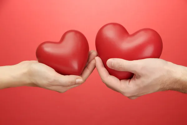 Rode harten in handen van vrouw en man, op rode achtergrond — Stockfoto