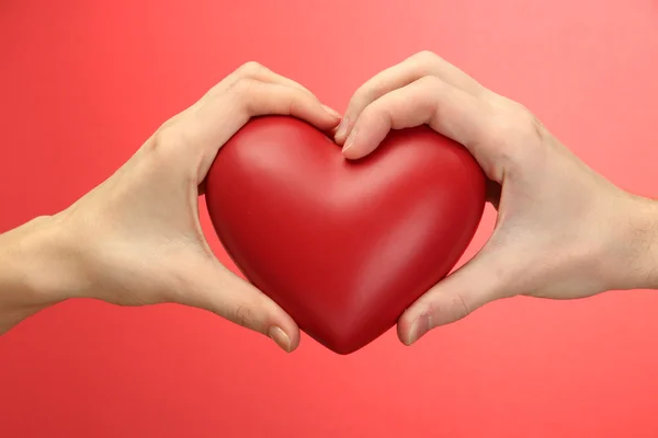 Rood hart in handen van vrouw en man, op rode achtergrond — Stockfoto