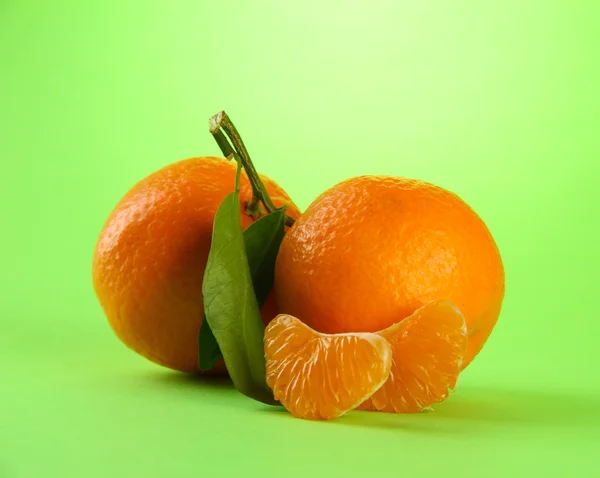 Спелые сладкие мандарины с листьями, на зеленом фоне — стоковое фото