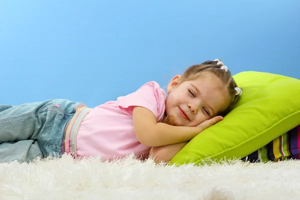 Schattig klein meisje slapen op kleurrijke kussens, op blauwe achtergrond — Stockfoto