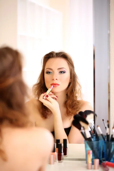 Jovem bela mulher fazendo maquiagem perto do espelho — Fotografia de Stock