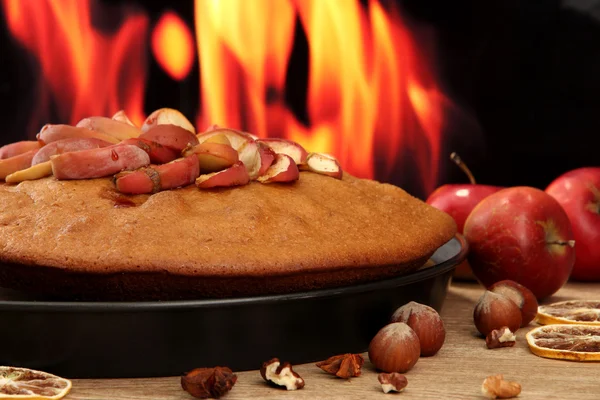 Sabroso pastel casero con manzanas y nueces, sobre una mesa de madera sobre fondo de llama — Foto de Stock