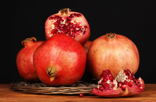 Ripe pomegranates on wicker cradle on black background — Stock Photo, Image