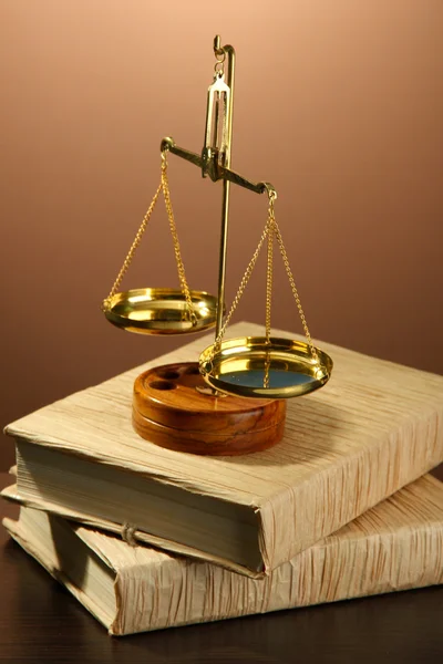 Gold scales of justice and books on brown background Stock Image