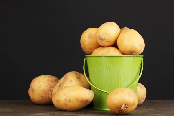 Ripe potatoes in pail on wooden table on black background — Stock Photo, Image