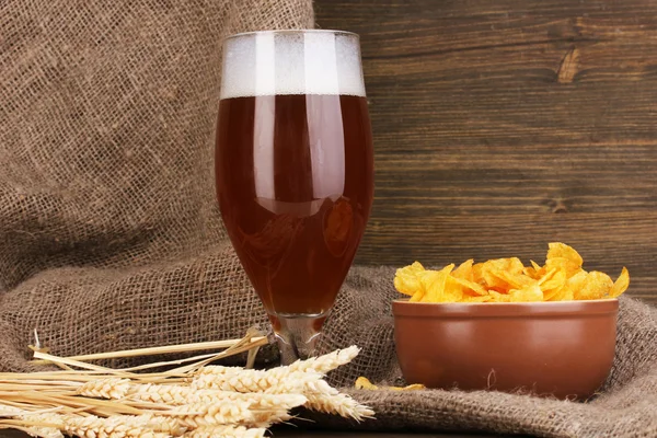 Verre de bière avec plaque de copeaux sur table en bois sur fond de sac — Photo