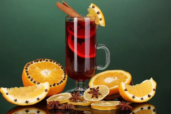 Duftender Glühwein im Glas mit Gewürzen und Orangen auf grünem Hintergrund — Stockfoto