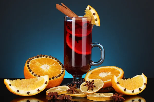 Fragrant mulled wine in glass with spices and oranges around on blue background — Stock Photo, Image