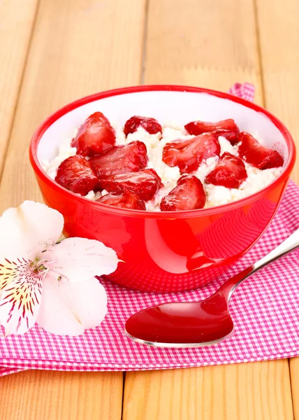 Hüttenkäse in roter Schüssel mit Erdbeeren in Scheiben auf Holztisch — Stockfoto