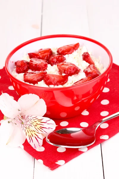 Cottage fromage dans un bol rouge avec des fraises tranchées sur table en bois blanc — Photo
