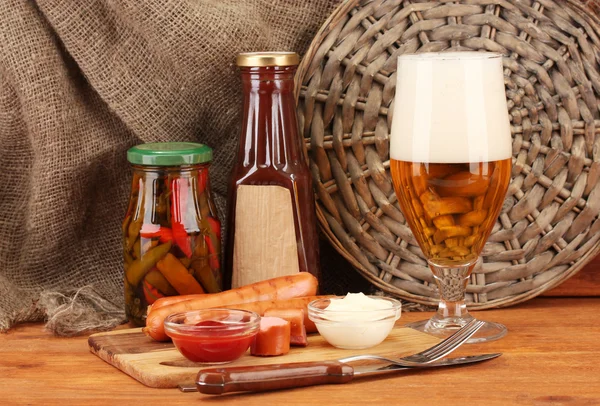 Bière et saucisses grillées sur table en bois sur fond de sac — Photo