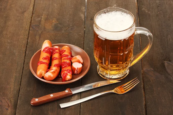 Cerveja e salsichas grelhadas em fundo de madeira — Fotografia de Stock