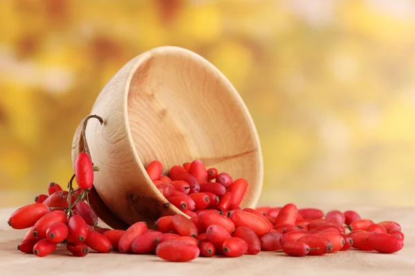 Ripe barberries in wooden bowl, on table, on yellow background — Stock Photo, Image