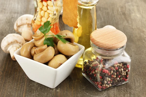 Heerlijke gemarineerde paddestoelen in kom met specerijen op houten tafel — Stockfoto