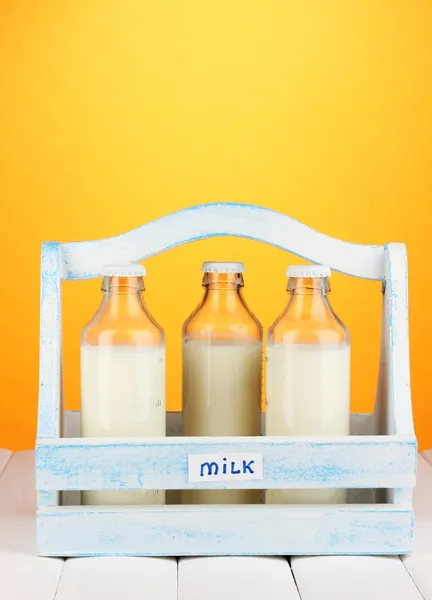 Milk in bottles in wooden box on wooden table on orange background — Stock Photo, Image