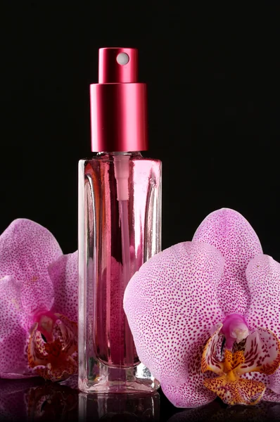 Frauenparfüm in schönen Flaschen und Orchideenblüten, auf schwarzem Hintergrund — Stockfoto