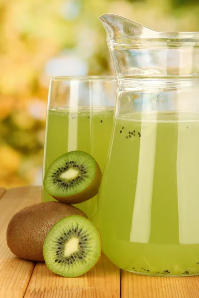 Full glass and jug of kiwi juice and kiwi on wooden table outdoor — Stock Photo, Image