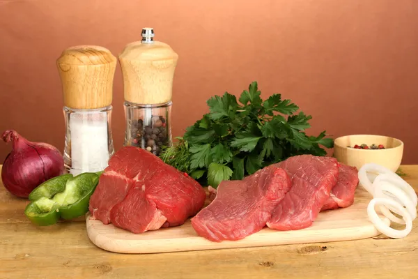 Raw beef meat with spices on wooden table on brown background — Stock Photo, Image