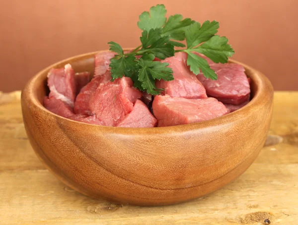 Raw beef meat in bowl on wooden table on brown background — Stock Photo, Image