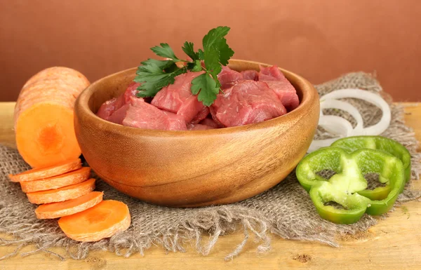 Carne de res cruda en tazón con verduras sobre mesa de madera sobre fondo marrón —  Fotos de Stock