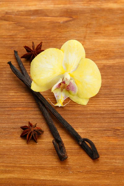 Vanilla pods and anise with flower, on brown wooden background