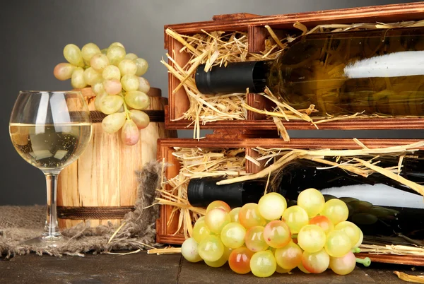 Caja de madera con botellas de vino, barril, vino y uva sobre mesa de madera sobre fondo gris — Foto de Stock