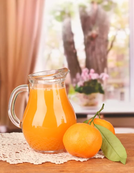Pełny dzbanek soku z mandarynki, na drewnianym stole na jasnym tle — Zdjęcie stockowe