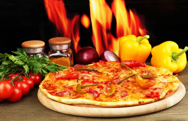 炎の背景に木の板に野菜と美味しいピーマンのピザ — ストック写真