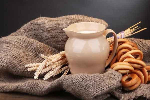Vaso di latte, gustosi bagel e spikelets su tavola di legno, su fondo grigio — Foto Stock