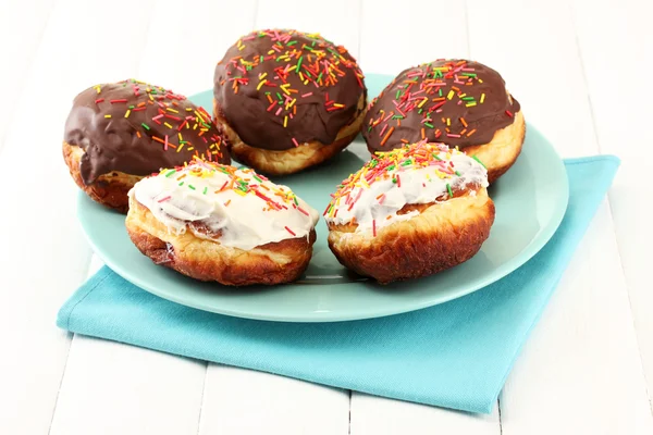 Tasty donuts on color plate on light wooden background — Stock Photo, Image