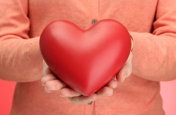 Corazón rojo en manos de mujer, sobre fondo rojo — Foto de Stock