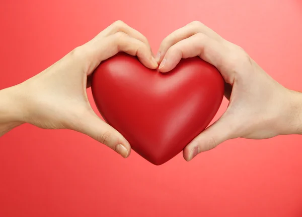Red heart in woman and man hands, on red background — Stock Photo, Image