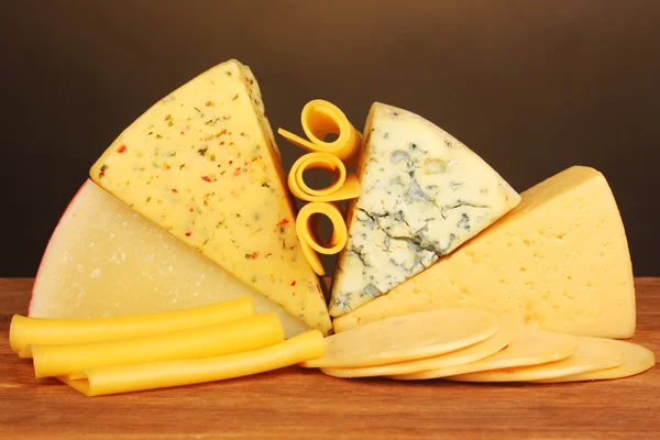 Verschiedene Käsesorten auf Holztisch auf braunem Hintergrund — Stockfoto