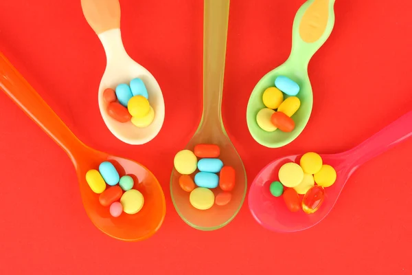 Plastic spoons with color pills on red background — Stock Photo, Image